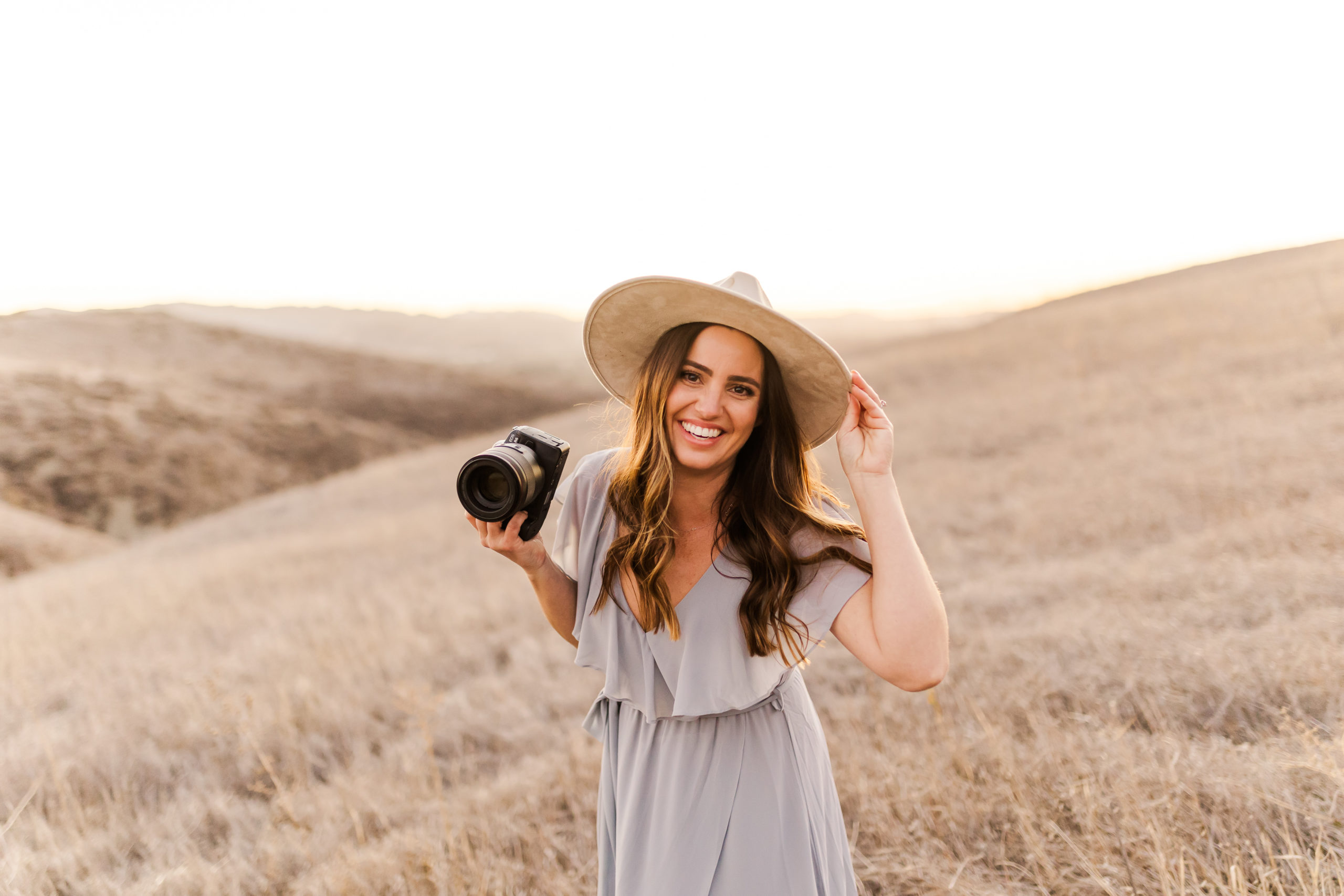 photographer wearing a hat and holding her camera laughing towards the camera